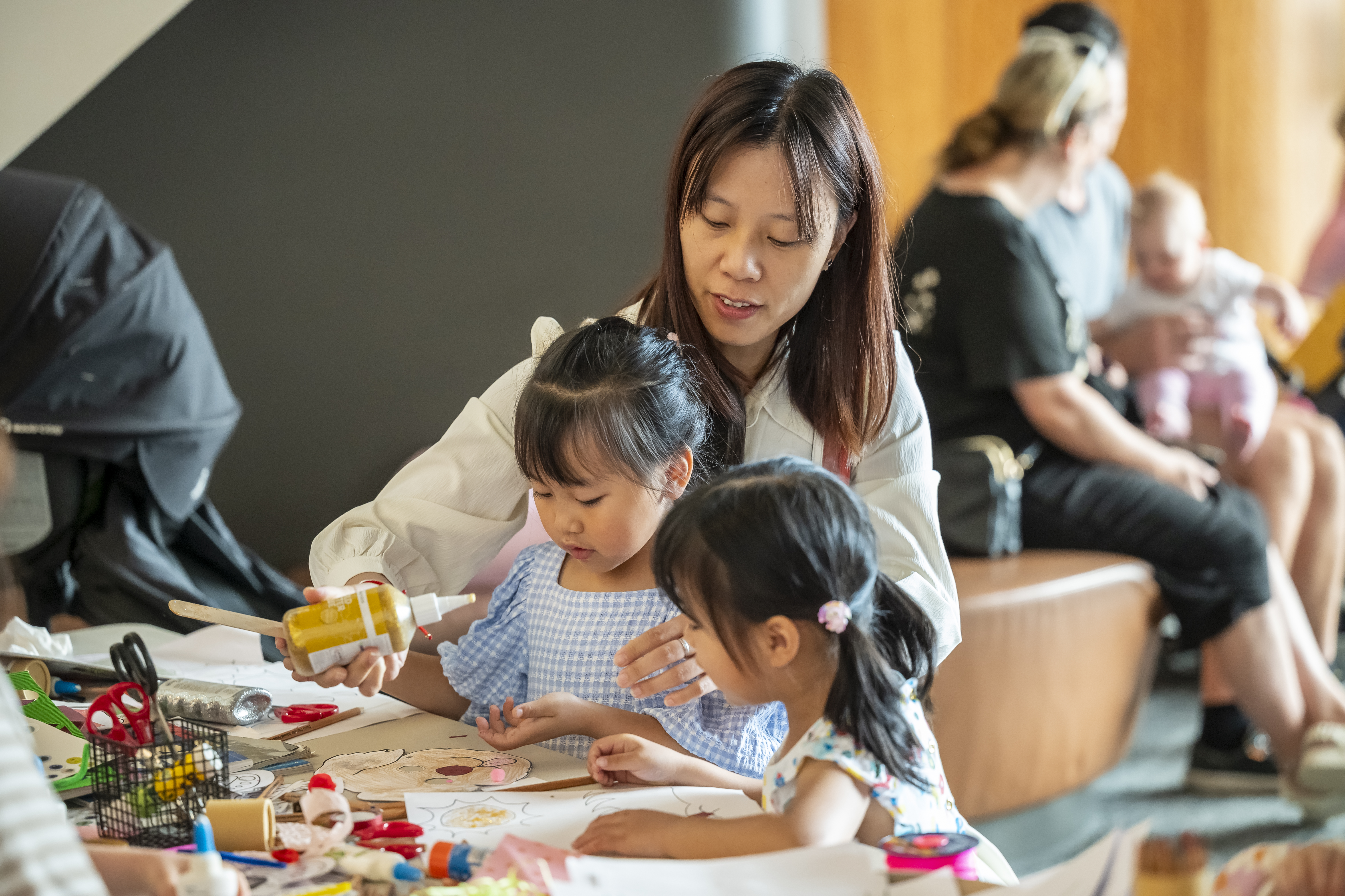 a woman helping two small children with art making