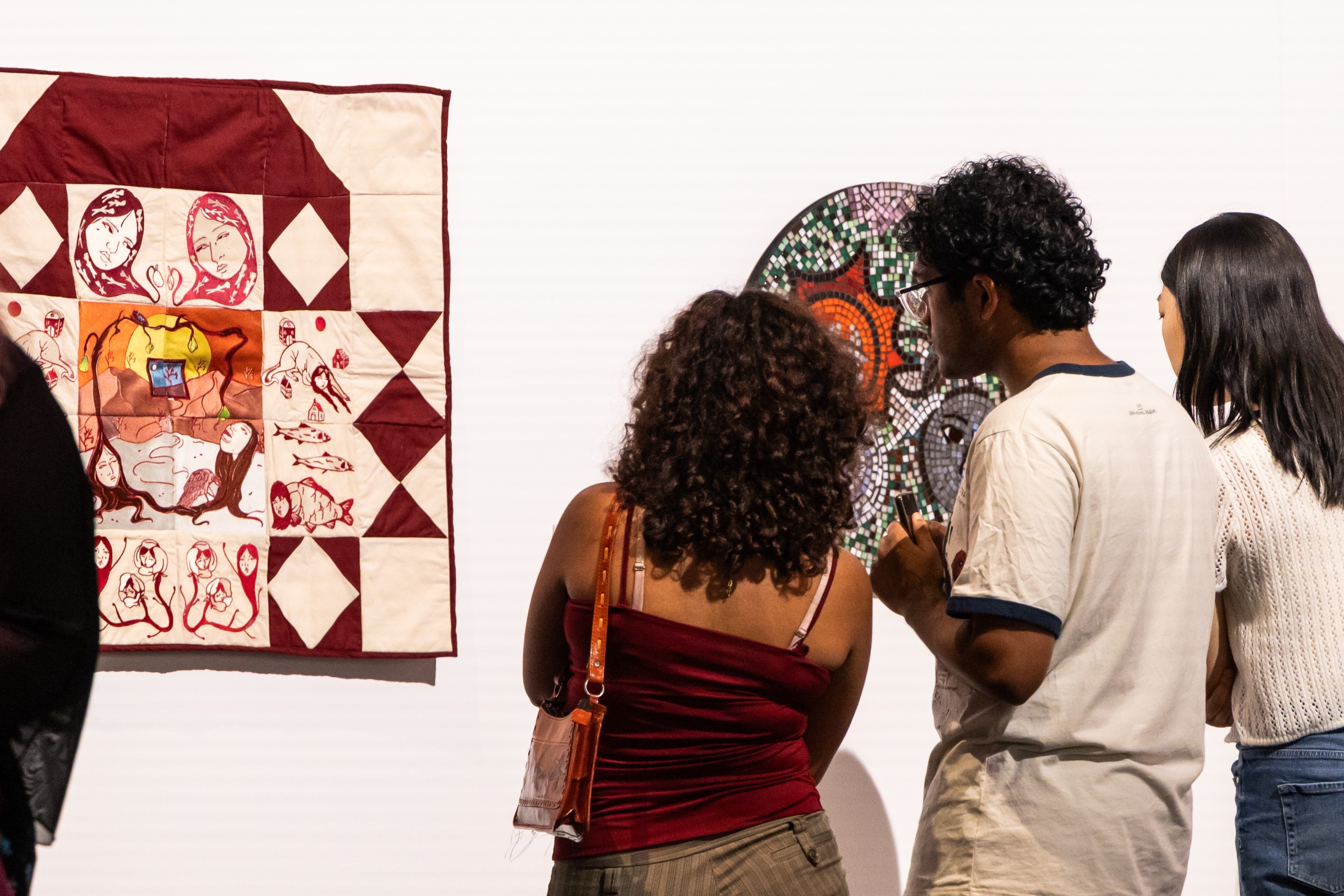 group of three people looking at a white and burgundy quilt 