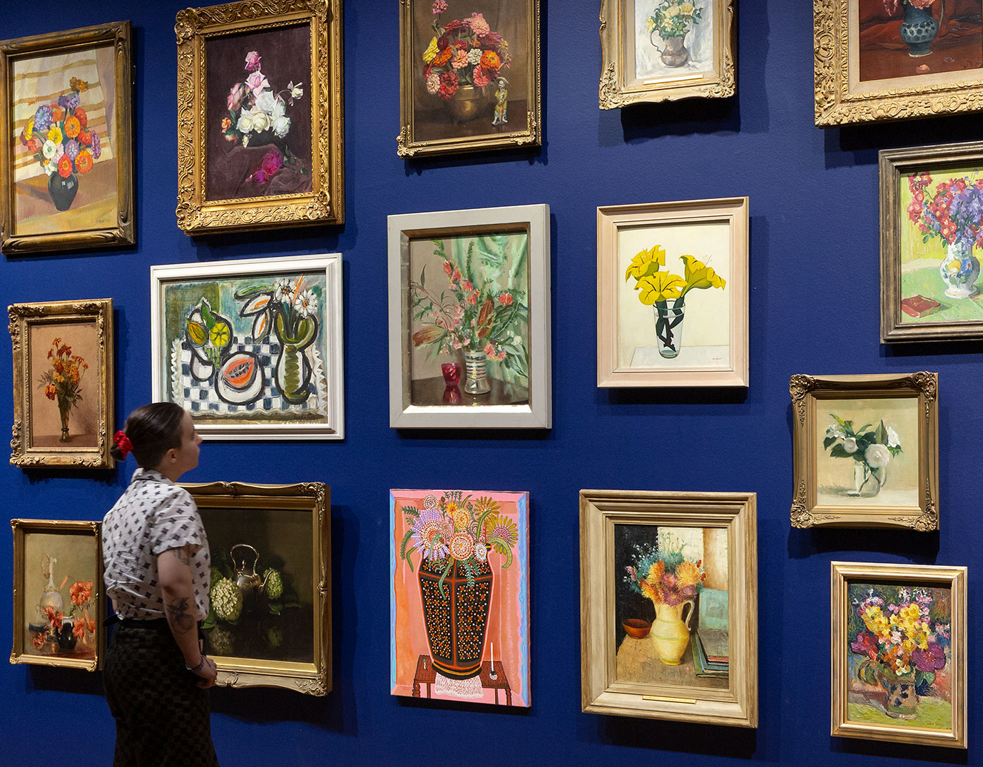 Salon hang of paintings with a person standing in front of the wall looking at the paintings