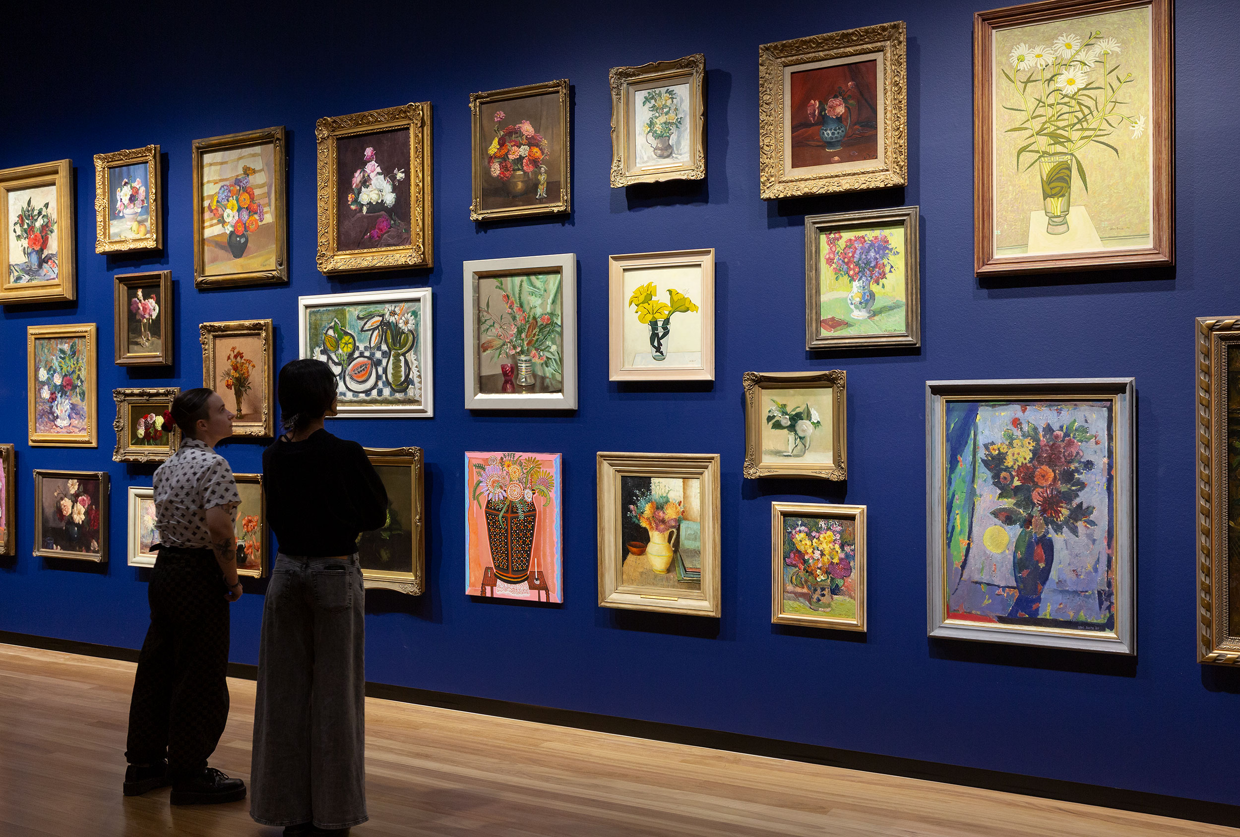 two people looking at a wall of paintings of flowers