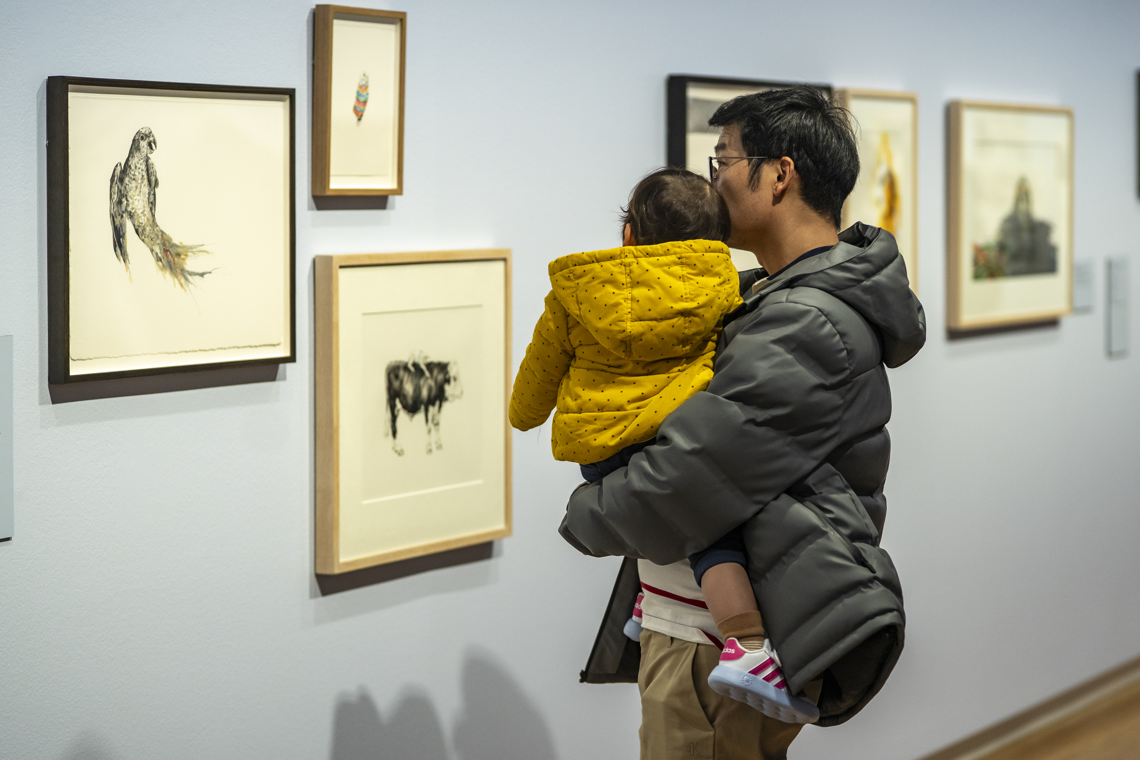 a parent holding a toddler looking at an artwork