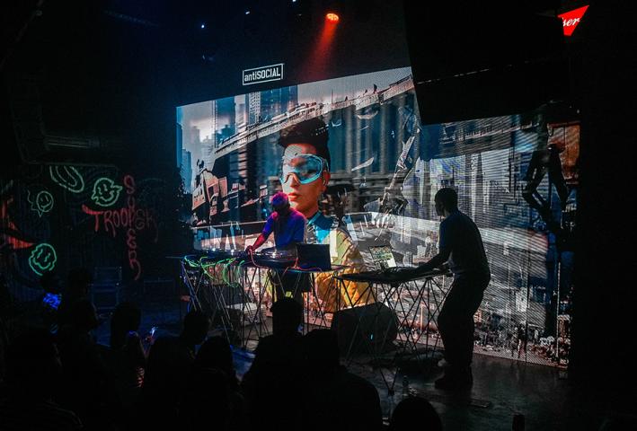 Two men DJing in front of a large screen with a crowd watching