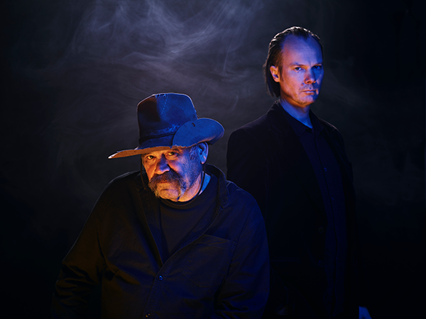 Two men in shadows look at the camera