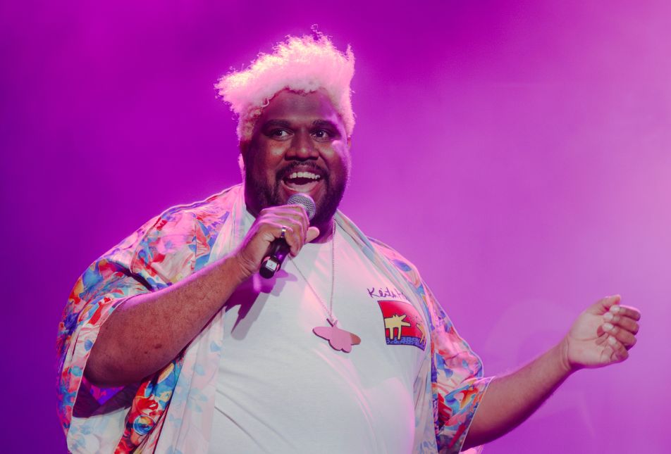 A man wearing a white printed shirt speaks into a microphone. 