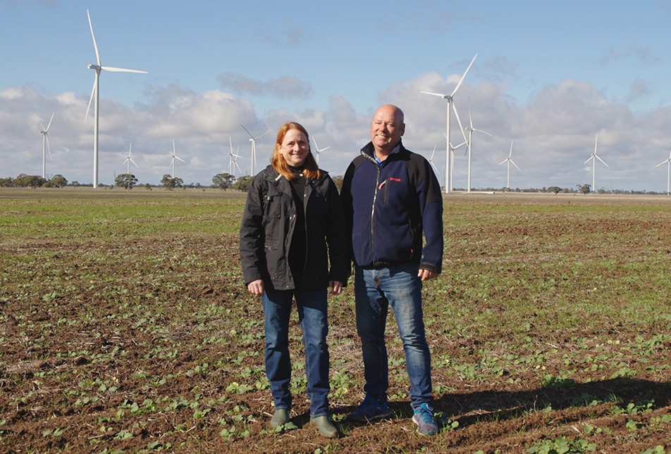 Two people standing in a field with wind generators behind them.