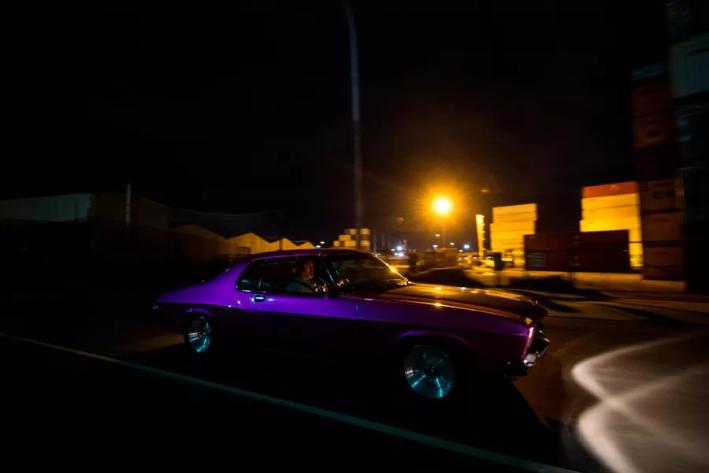 A purple car driving along a dark road.