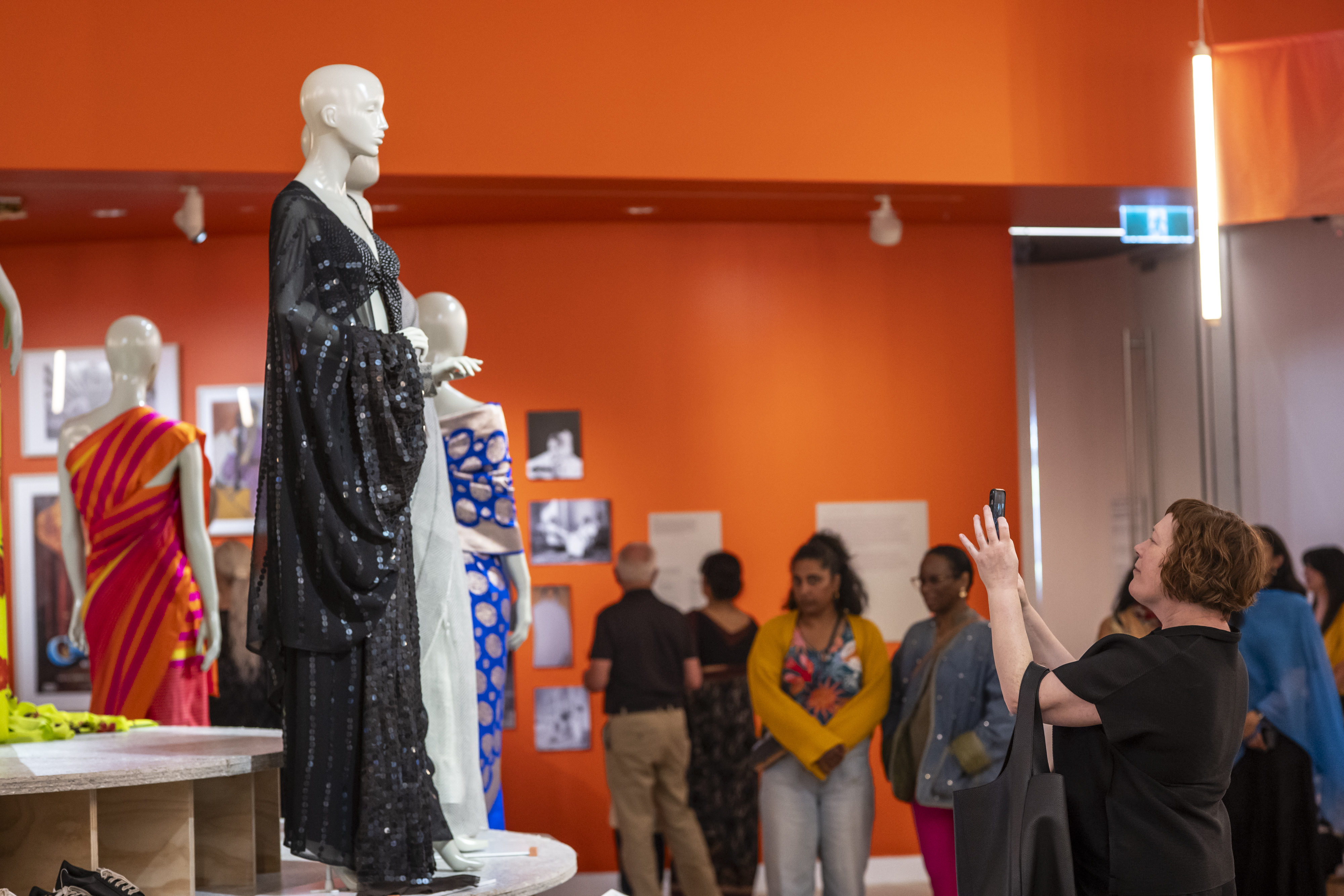 People walking about an art gallery with saris on display.