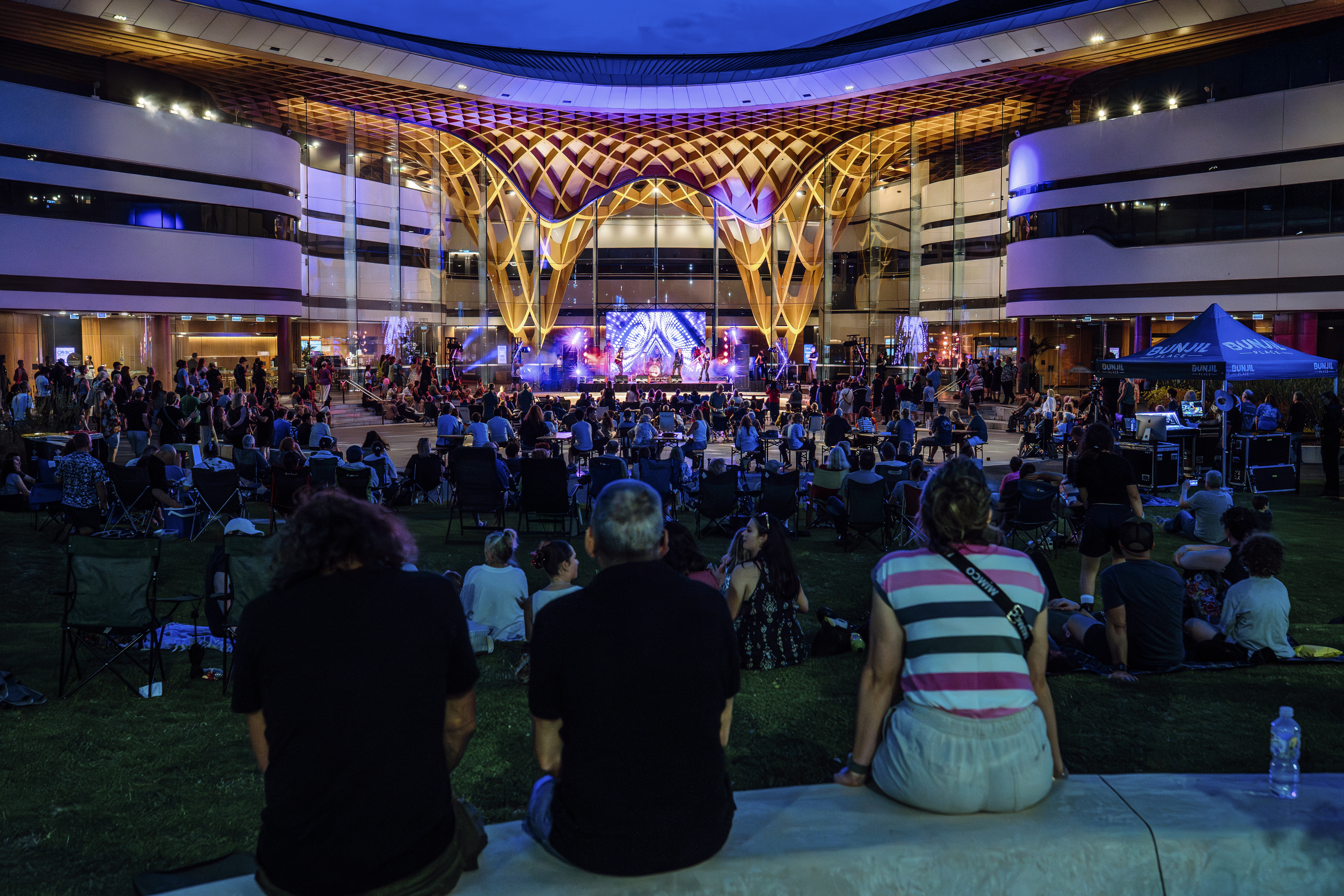 A large crowd of people watching a rock band under the Bunjil PLace PLaza gridshell