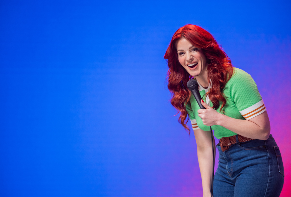 A woman with red hair and wearing a green shirt holds a microphone