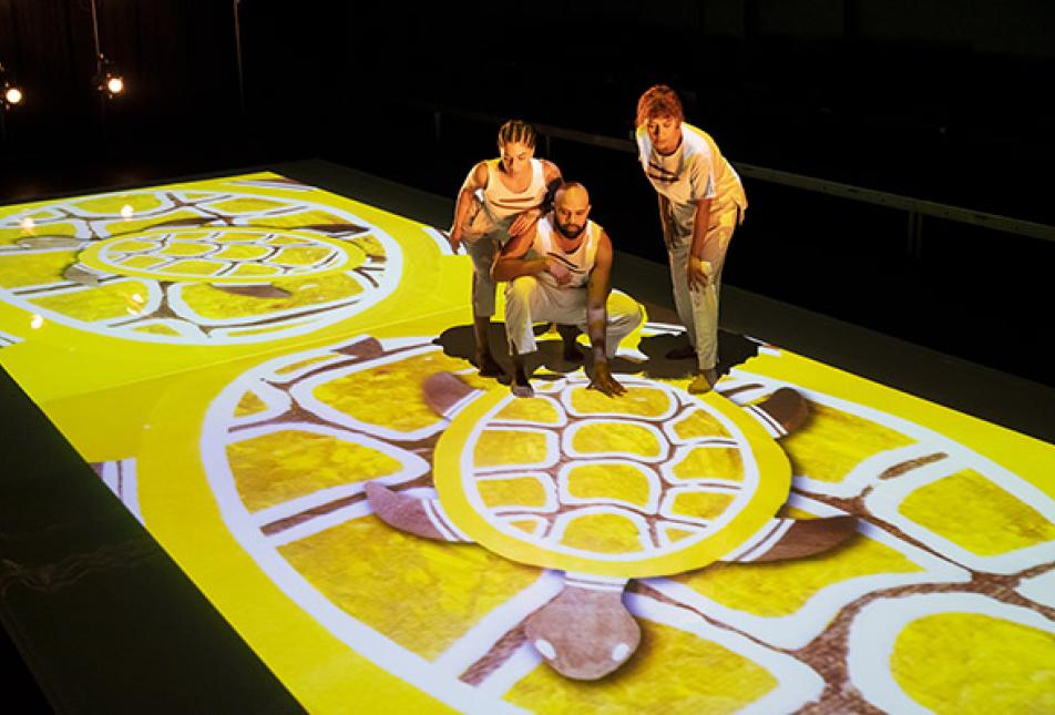 Performers stand on a floor lit by digital images 