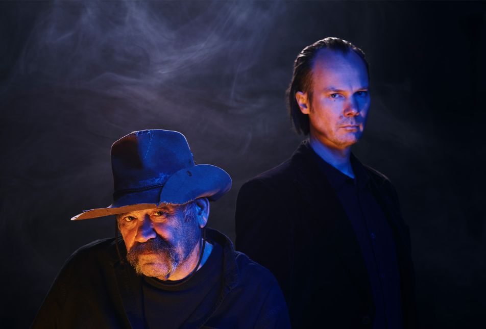 Two men stand in a dark smoky background