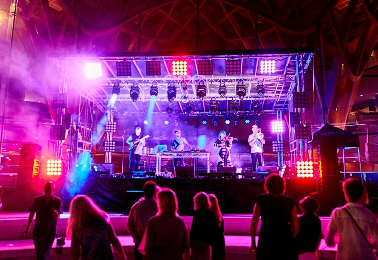 musicians playing on an open air stage under lights at Bunjil Place.