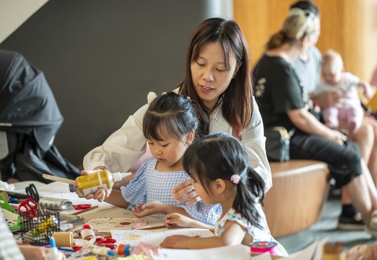 a woman helping two small children with art making