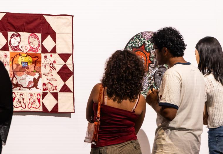 group of three people looking at a white and burgundy quilt 