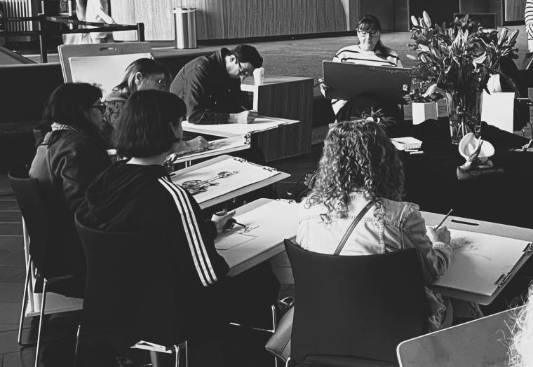 group of people sitting down drawing a still life display