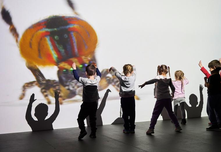 children dancing in front of a large projection of a spider