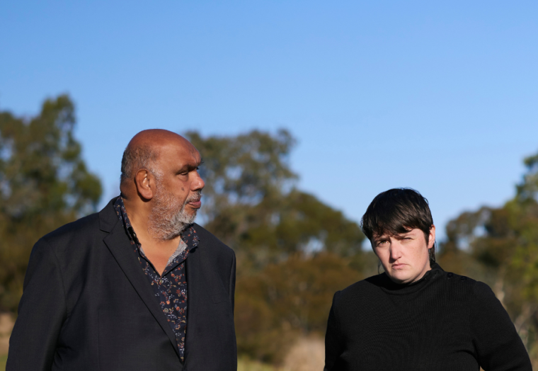 Two men in black shirts stand in bushland