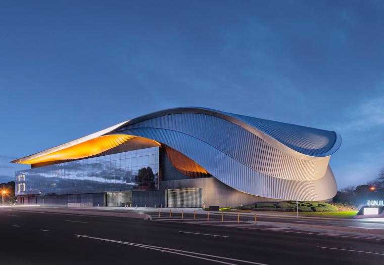 The external view of the Bunjil Place precinct from the road - a large, sweeping metal gridshell across two stories of windows.