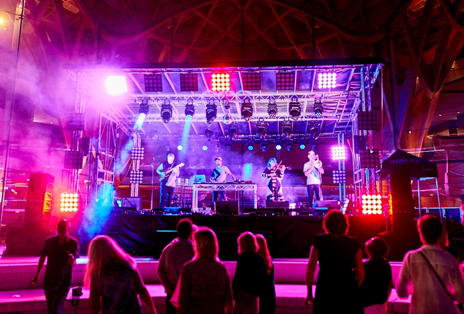 musicians playing on an open air stage under lights at Bunjil Place