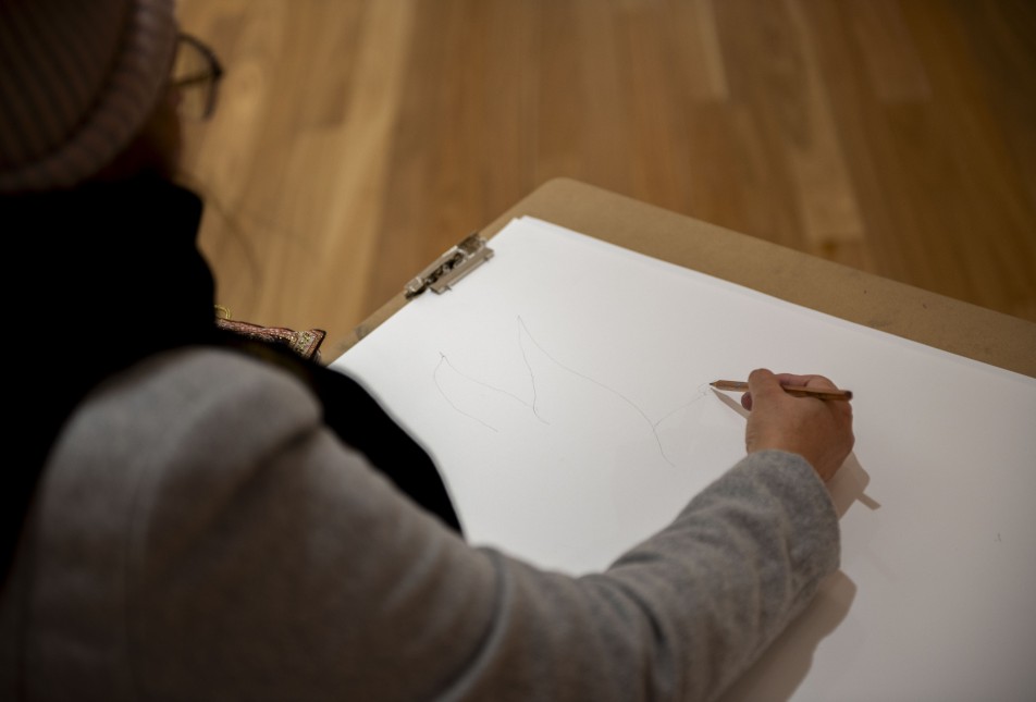person wearing grey jacket sketching on white paper using a grey lead pencil