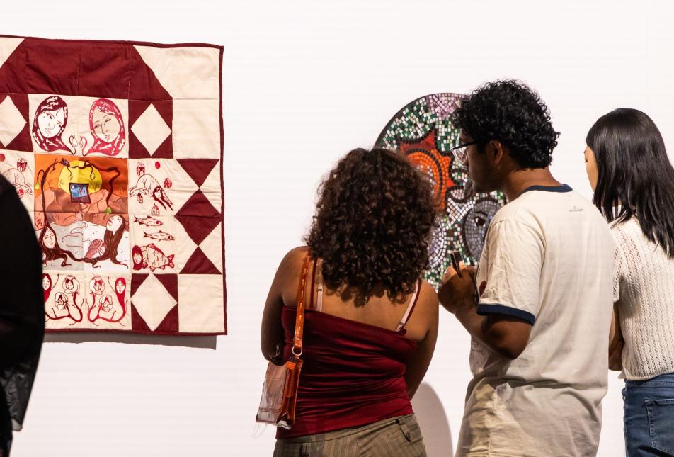 group of three people looking at a white and burgundy quilt 