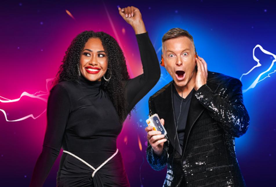 A woman in a black dress dances with her hand up in the air while a man in a suit has a surprised look on his face. 