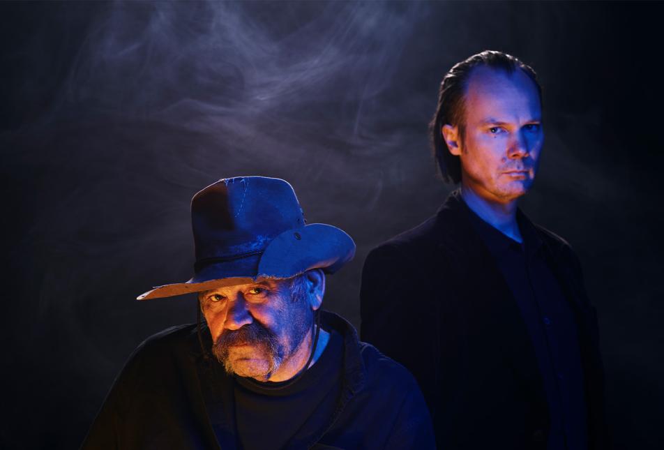 Two men in shadows look at the camera