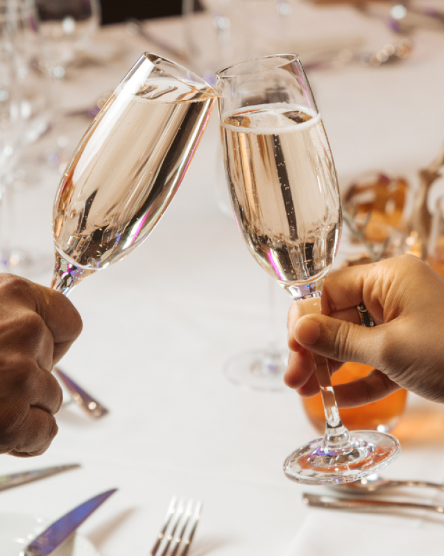 A table setting including two hands toasting with a glass of wine each