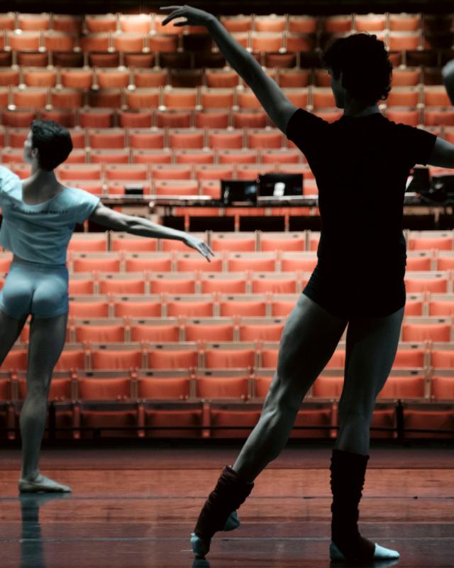 Silhouette of ballet dancers rehearsing on stage, in front of an empty theatre