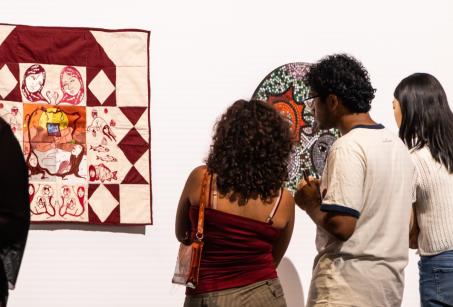 group of three people looking at a white and burgundy quilt 