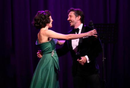 A woman in a green dress hugs a man in a black suit