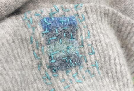 Visible mending of a grey cloth using blue stitching