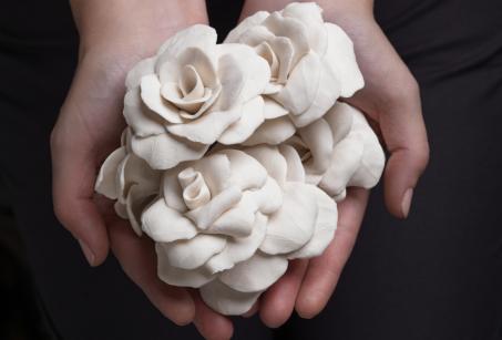 Hands cupped together holding a group of white porcelain flowers by Jess Dare