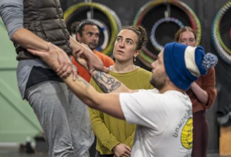 A man lifts up another watched on by other circus performers