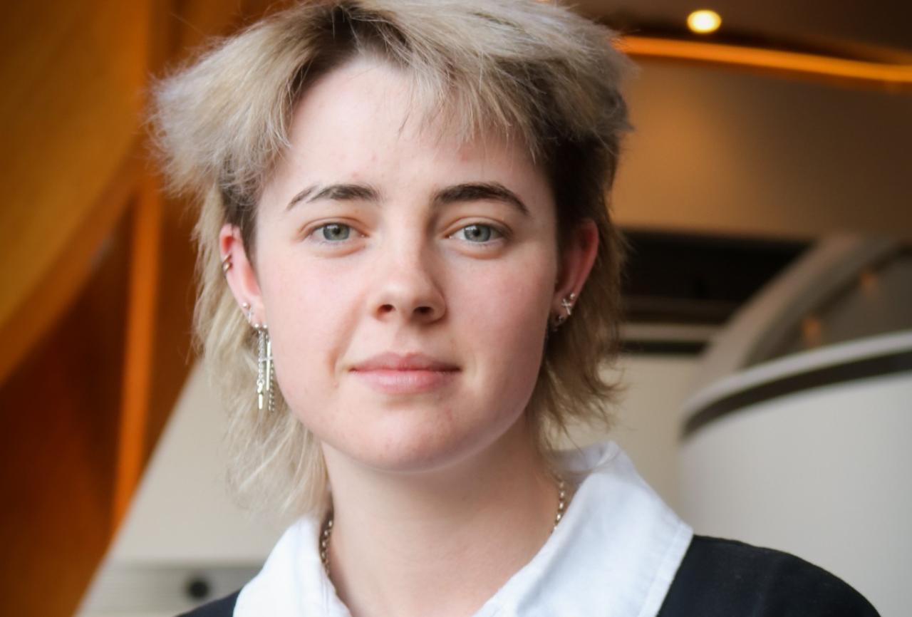 Young person with blonde hair wearing a white and black polo