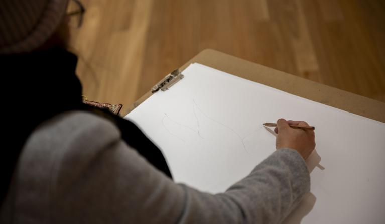 person wearing grey jacket sketching on white paper using a grey lead pencil