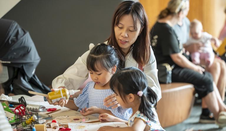 a woman helping two small children with art making