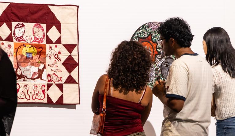 group of three people looking at a white and burgundy quilt 