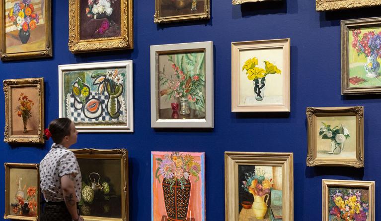 Salon hang of paintings with a person standing in front of the wall looking at the paintings