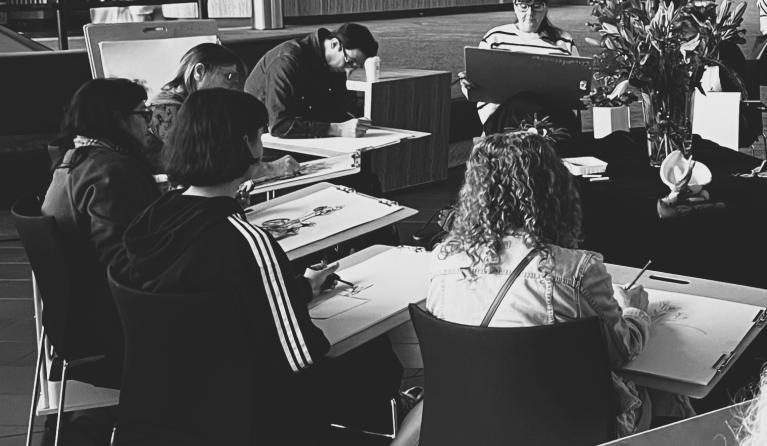 group of people sitting down drawing a still life display
