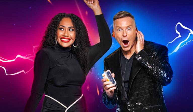 A woman in a black dress dances with her hand up in the air while a man in a suit has a surprised look on his face. 