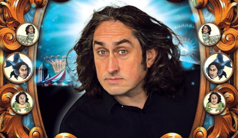 A man with long dark wavy hair looks through a frame that features buttons with his face on creatures - Ross Noble Cranium of Curiosities