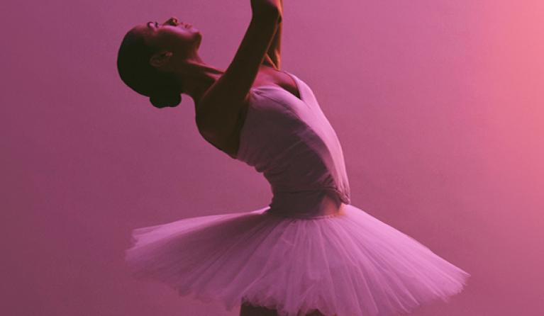 A ballet dancer in a tutu against a pink lit background
