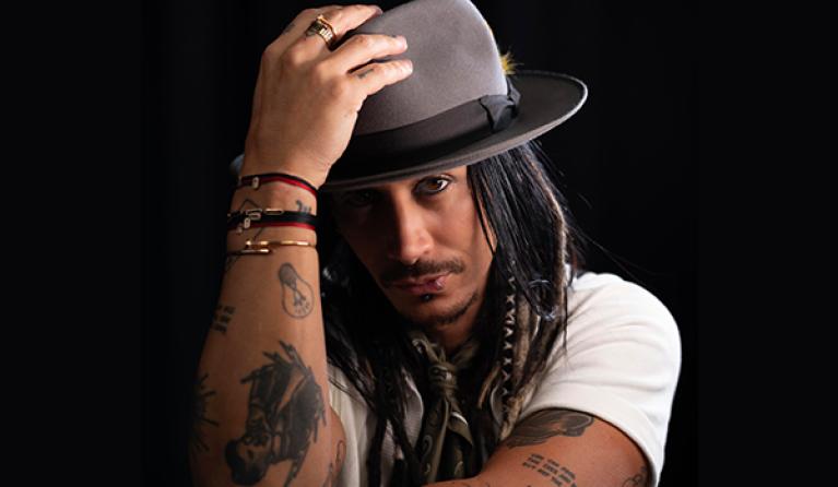 A man in a white t-shirt holds a hat on his head