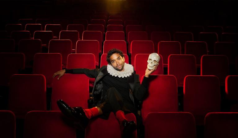 A man sits in a theatre holding a skull. 