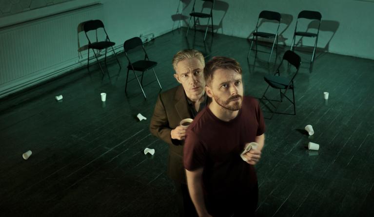 Two men stand in a room, looking up at a security camera