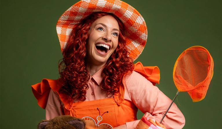 A woman with curly red hair wearing an orange dress smiles up at the camera