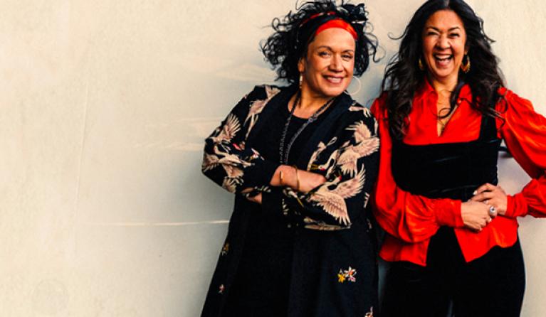 Two women with long dark hair smile at the camera. 