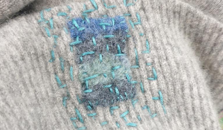 Visible mending of a grey cloth using blue stitching