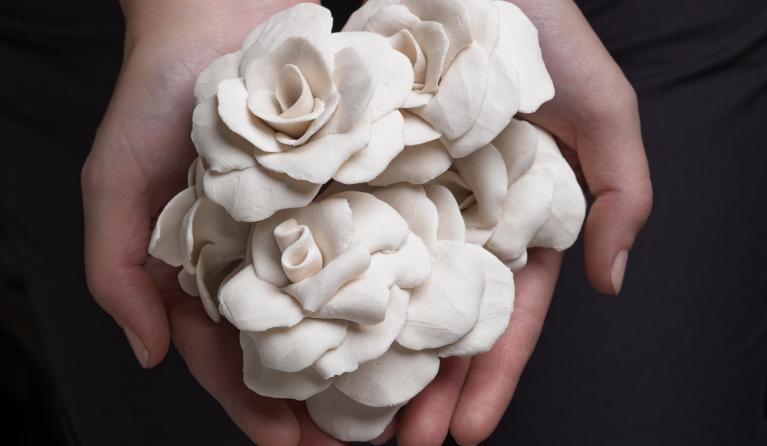 Hands cupped together holding a group of white porcelain flowers by Jess Dare